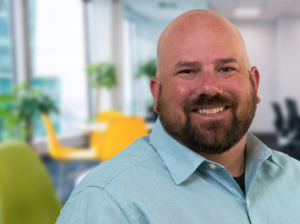 Brandon - portrait of bald man with beard smiling in light blue shirt